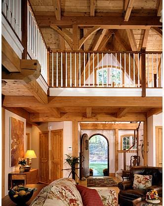 arched front door opening into timber frame great room with balcony above